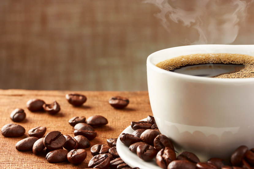 steaming cup of coffee surrounded by coffee beans